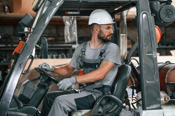 Driving the forklift. Young factory worker in grey uniform