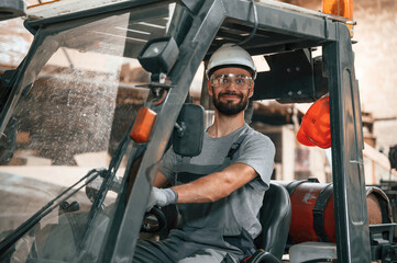 Naklejka premium Driving the forklift. Young factory worker in grey uniform