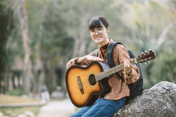 happy asian teen playing guitar music entertainment outdoor travel in the park