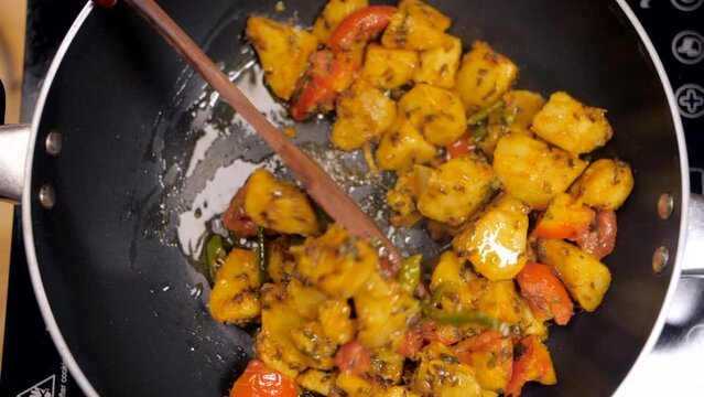 Indian kitchen - cooking vegetarian food  Jeera Aloo in a non-stick pan  delicious food  home-cooked food. Popular Indian dish prepared with boiled potatoes  and tomatoes seasoned with cumin seeds ...