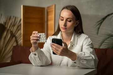 A female customer uses a mobile phone, holding a box of medicines while sitting at a table. 