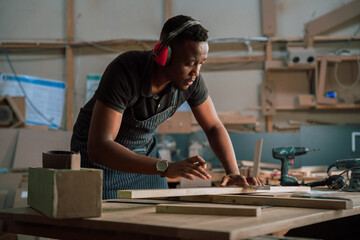 Focused African male draws pencil mark for measurement on carpentry project  - obrazy, fototapety, plakaty