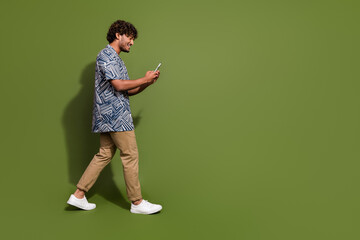 Full length photo of cool good mood guy wear print shirt communicating modern device empty space isolated khaki color background