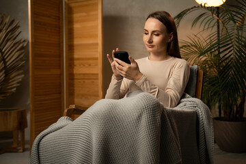 Smiling woman using mobile phone while sitting at home. 