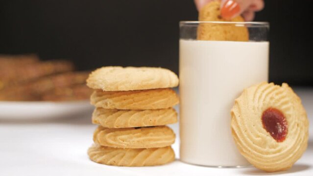 Female hand dipping a toasted rusk in a glass of warm milk - breakfast  dairy products  gluten-free  lactose-free. Dunking toast in fresh almond milk - enjoying nutritious snack  instant energy boo...