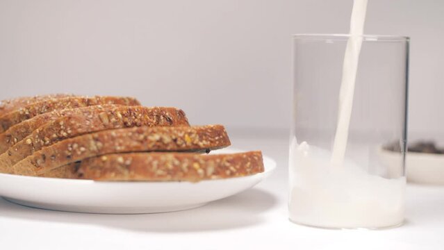 Milk is poured into a transparent glass for breakfast - rich in nutrients  calcium  vitamin D. Closeup shot of freshly baked multigrain bread and warm milk - nutritious  dairy product  dietary fibe...