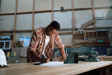 Focused African male uses pen for designing woodwork project - obrazy, fototapety, plakaty