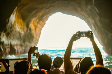 Tourist sightseeing and taking photos with smartphones inside the cave on Algarve coast, Albufeira,...