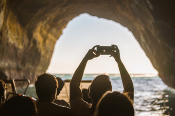 Tourist sightseeing and taking photos with smartphones inside the cave on Algarve coast, Albufeira, Portugal