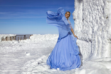 Beautiful elegant woman wearing blue fluttering long dress and is posing on a sunny day in the mountains. Snow queen.
