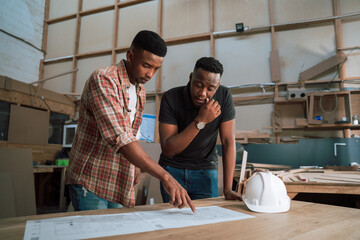 Male African American colleagues discuss plans in carpentry warehouse 