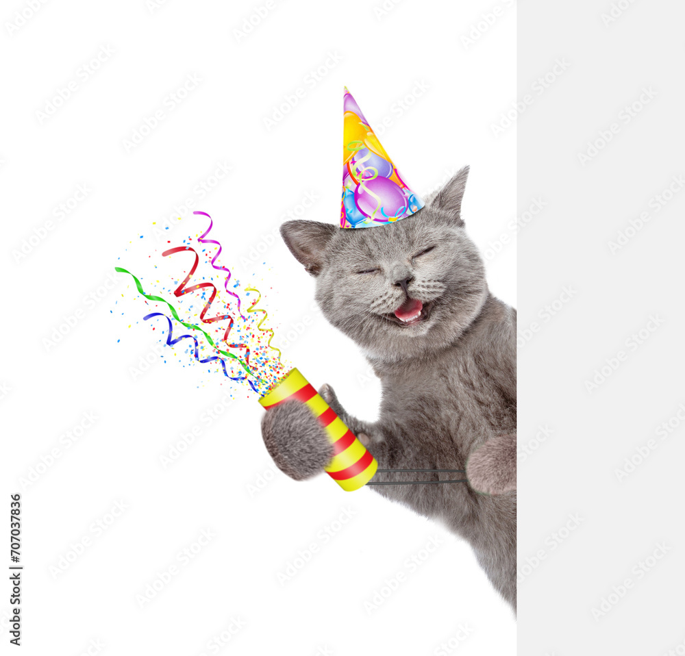 Poster Happy cat wearing party cap holds exploding firecracker and looks from behind empty white banner. Isolated on white background