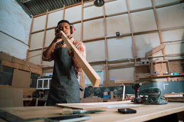 Young African male with earmuffs checks level of piece of wood in carpentry factory 