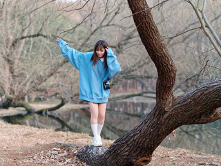 Beautiful young Chinese woman posing in sunny summer forest, wearing blue loose oversized top and miniskirt with small shoulder bag. Emotions, people, beauty, youth and lifestyle portrait.