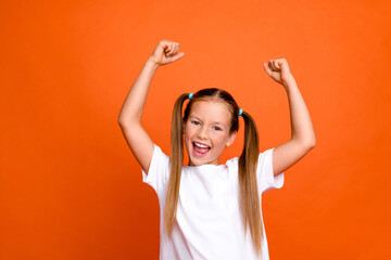Photo portrait of charming little girl raise fists excited scream yes lucky wear trendy white clothes isolated on orange color background