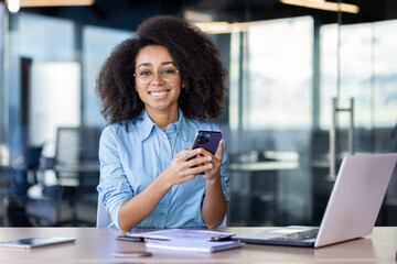 Portrait of young office worker with phone in hands, businesswoman smiling and looking at camera,...