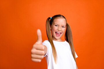 Photo portrait of charming little girl show cheerful thumb up wear trendy white clothes isolated on orange color background