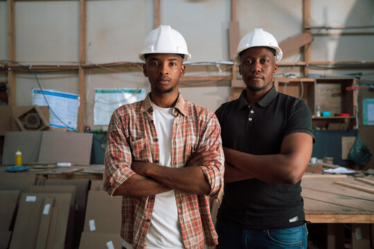 Two serious African Americans with hardhats pose for picture in woodwork warehouse 