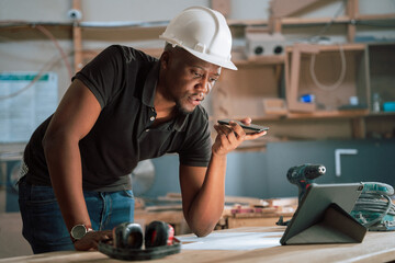African American male speaks on phone while looking at designs on tablet in woodwork warehouse