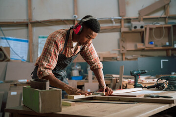 Concentrated African male wearing earmuffs measures piece of wood for carpentry project 
