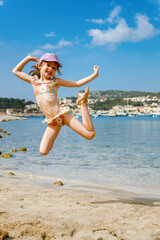 Happy little girl in a swimsuit jumping on the beach