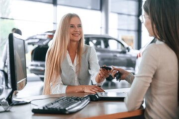 Giving the keys. Female manager is helping woman customer in the car dealership salon - Powered by Adobe