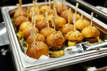 A platter of savory mini burgers with toothpicks and condiments