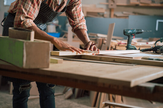 Medium shot of African American male with pencil drawing a mark on wood in carpentry factory 