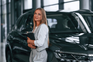 Fototapeta na wymiar Leaning on the automobile. Woman in formal clothes is in the car dealership
