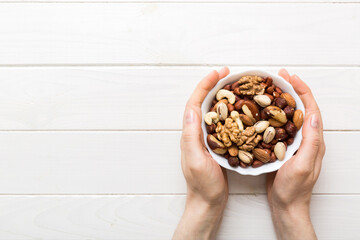 Woman hands holding a wooden bowl with mixed nuts Walnut, pistachios, almonds, hazelnuts and...
