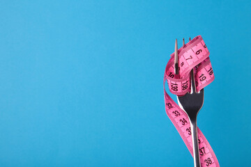Measuring tape wrapped around fork on blue background. Diet concept