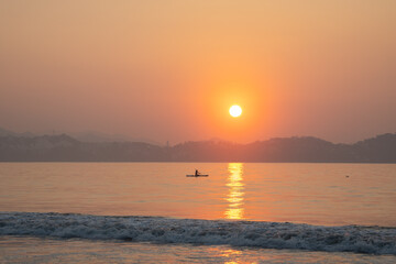 Naklejka premium paddlesurf deporte practicado en el mar en el océano en la playa deporte extremo relajante rodeado de tranquilidad en un hermoso atardecer con la puesta del sol brillante y al horizonte montañas