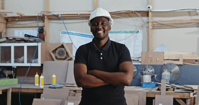 Young African male wearing hardhat poses for video in a carpentry factory 