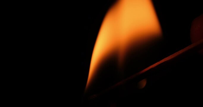 Hand Lights Paraffin Candle using a Match, Black Background. Bright flame, fire, ignition in a dark room