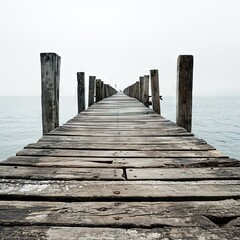 Fototapeta premium An old wooden pier extends into the mist waters of the lake. A solitary path towards the calm and peaceful silence of nature, with the sweet sound of the waves.