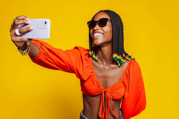 Smiling african woman with braided hairstyle and sunglasses, holds modern mobile phone in front of...