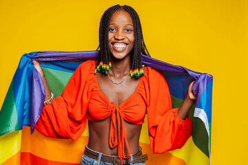 African american young smiling girl with braids, toothy smiles with pride rainbow flag at studio isolated over yellow background. Trans or bisexual concept. - obrazy, fototapety, plakaty