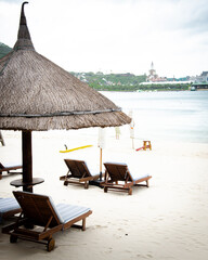 White sandy beach with empty lounge chair covered by beach umbrella thatched palm leaves, on quite...