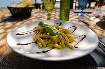 A plate of penne pasta on Sardinia, adorned with pesto, drizzled with balsamic vinegar, and garnished with fresh basil leaves.