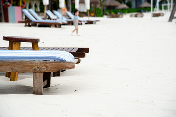 Close-up empty beach lounge chairs and collapsed umbrella on white sandy beach in early morning at...