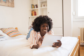 Happy woman using digital tablet while lying in bed at home