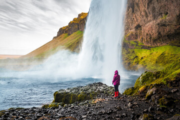 Tourist person in red raincoat watching Seljalandsfoss waterfall in Iceland - obrazy, fototapety, plakaty
