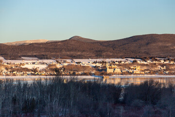 
Row of trees seen in winter, with the St. Lawrence River and the Ste. Anne-de-Beaupre basilica at the foot of the Laurentian mountains in soft focus background, Sainte-Famille, Island of Orleans