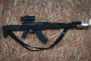 An AKM tactical rifle with a silencer, a weapon flashlight and a prismatic sight hangs on the wall...