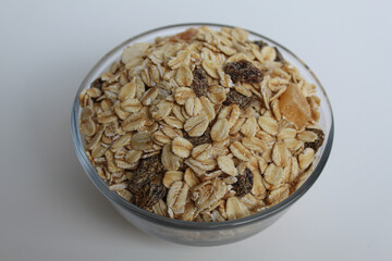 Muesli is rolled oats mixed with nuts, seeds, and dried fruits. In a transparent bowl, isolated on white background