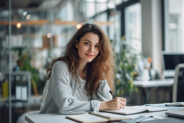Successful and happy business woman looking at camera sitting inside office working with documents, portrait of satisfied woman writing in notebook