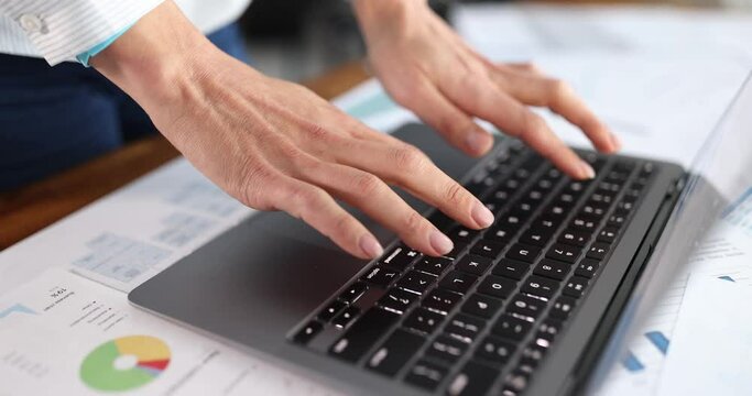Female hands typing on laptop keyboard among documents with graphs closeup 4k movie slow motion. Remote work in business concept