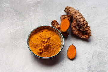 Turmeric powder in bowl and fresh turmeric root on textured background with space for text. Natural antioxidant close up photo. 