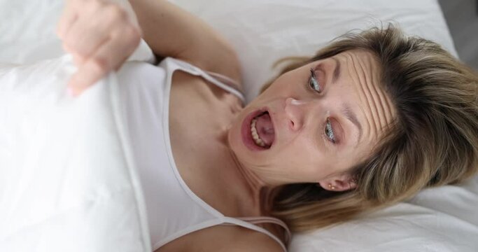 Frightened young woman lies in bed and looks under covers. Urinary incontinence at night in women concept