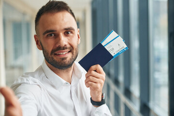 Smiling, holding tickets. Young handsome man in the airport